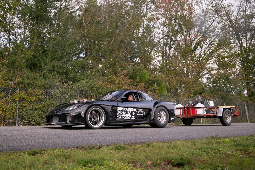 The black Veilside RX-7 towing a loaded utility trailer on the road